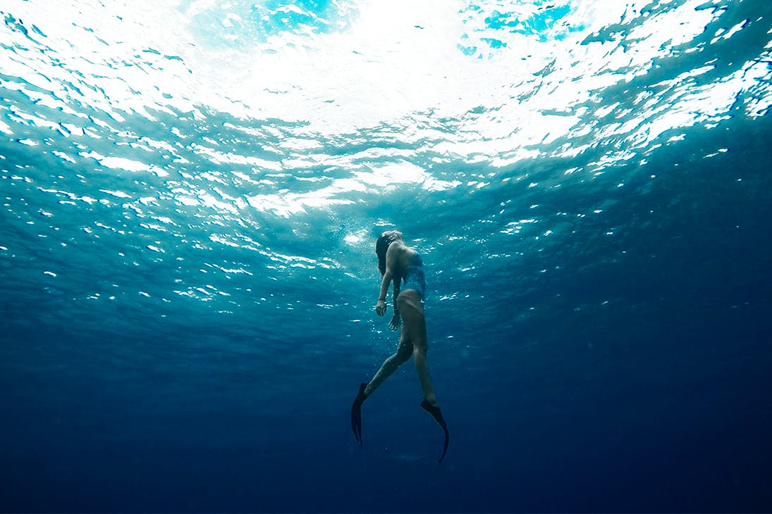 a woman swims towards the surface of the ocean.